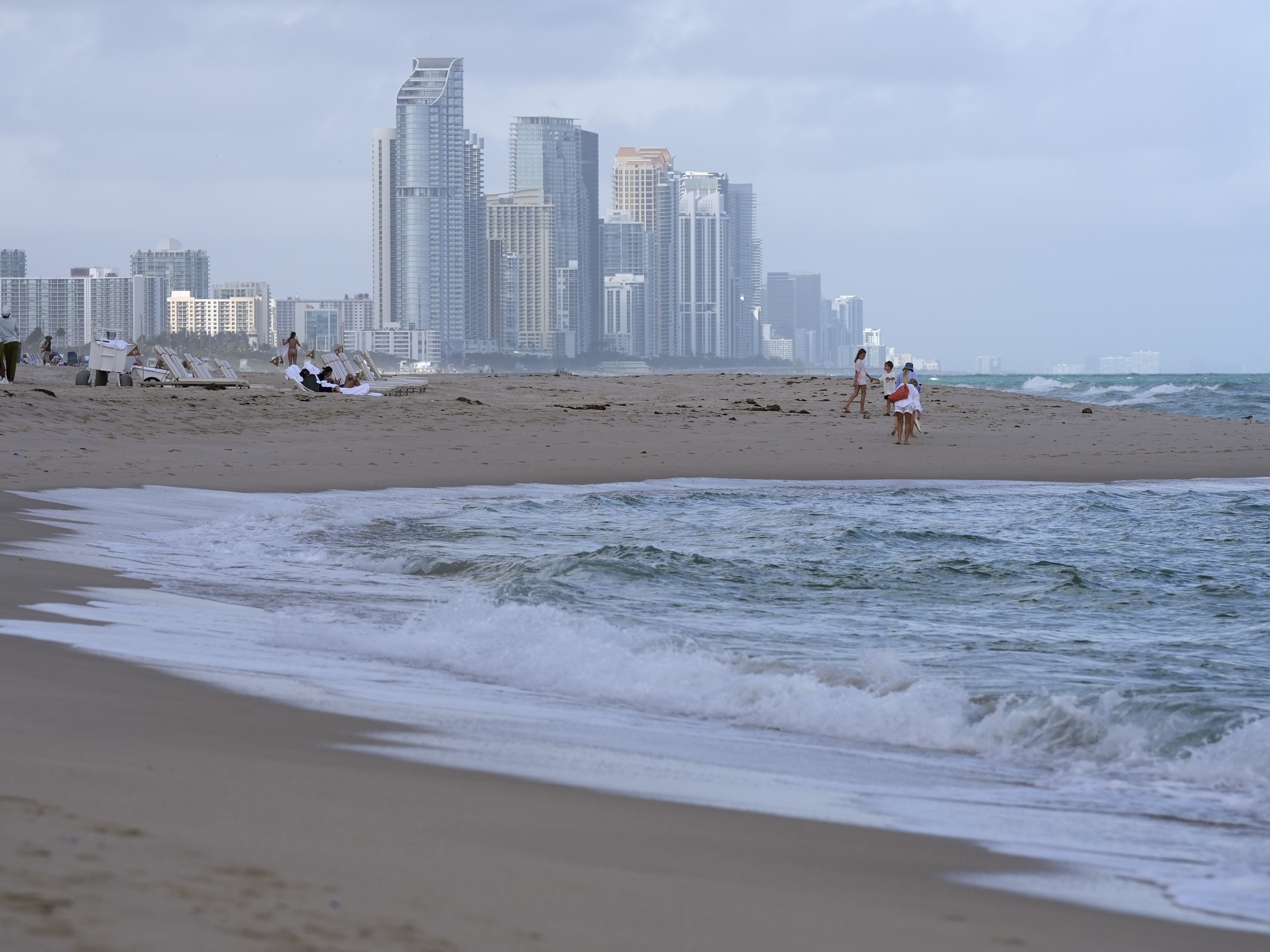 People walk along the beach in Surfside, Fla., near the skyline of Sunny Isles Beach, on Dec. 17, 2024.